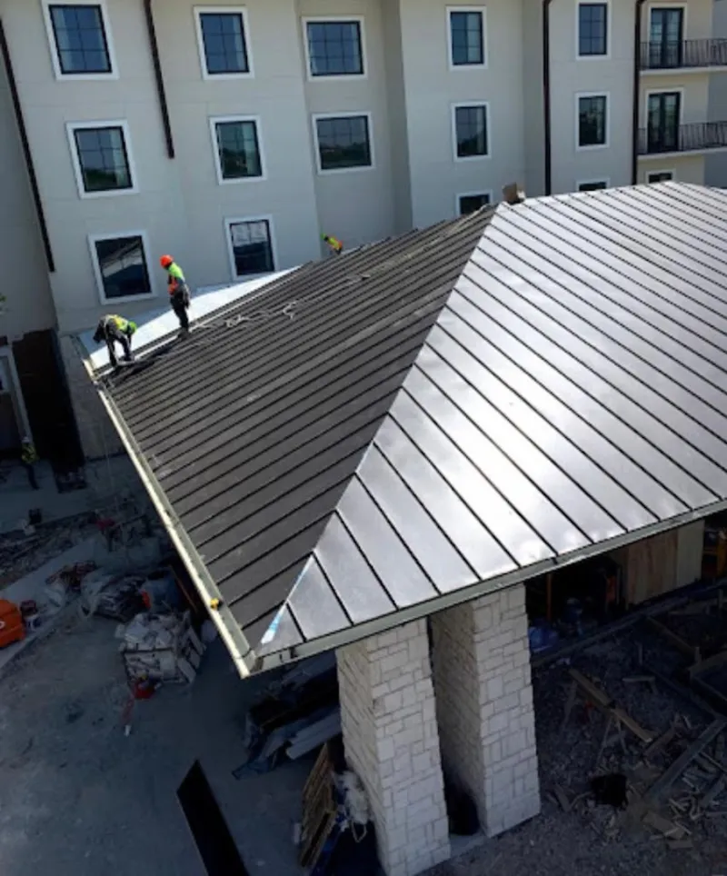 Crew installing standing seam metal roof panels on a commercial project in Janesville